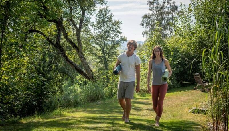 zwei Menschen mit Yogamatte gehen auf der Wiese