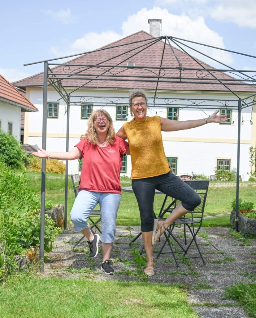 Zwei Frauen im Garten, fröhlich posierend.