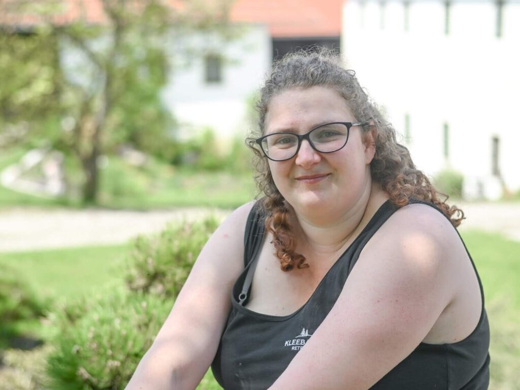 Frau sitzt im Garten, lächelt.