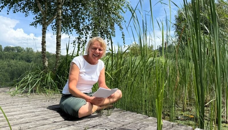 Frau sitzt am Wasser und liest.