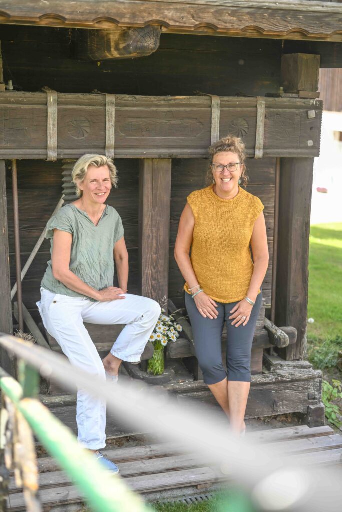 Zwei Frauen vor einem Holzgebäude.