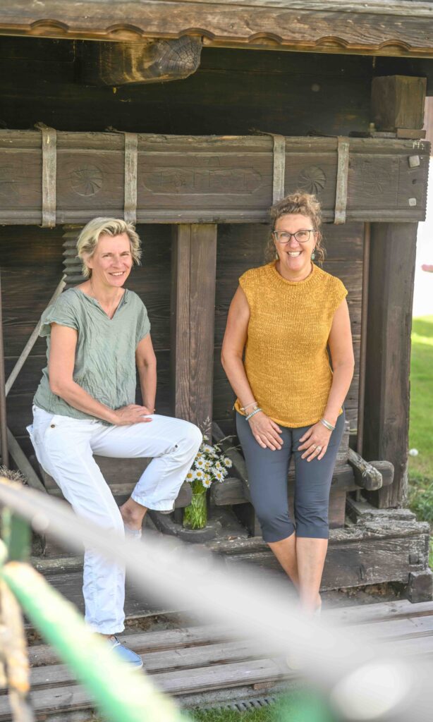 Zwei Frauen vor einem Holzgebäude.