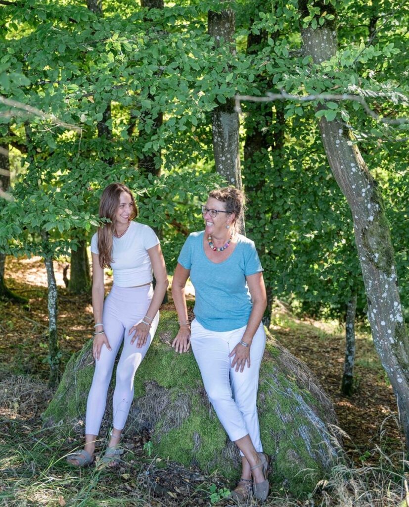 Zwei Frauen im Wald auf einem Baumstumpf.