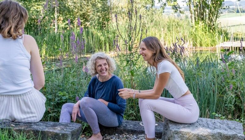 Frauen sitzen am Teich und lachen.