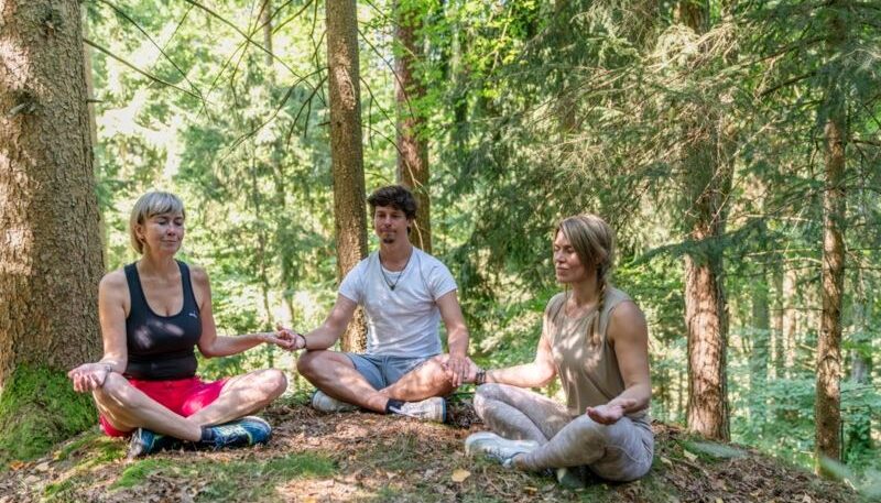 Drei Personen meditieren im Wald.