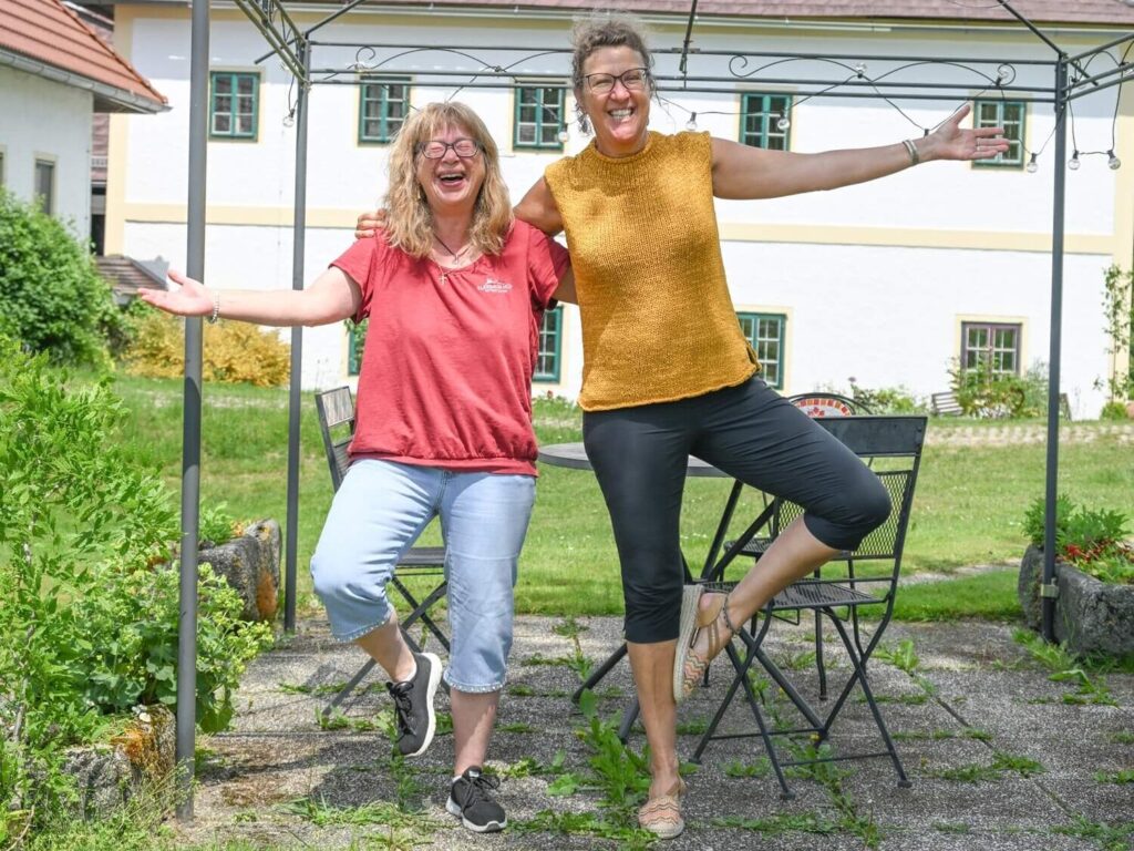 Zwei Frauen posieren fröhlich im Garten.
