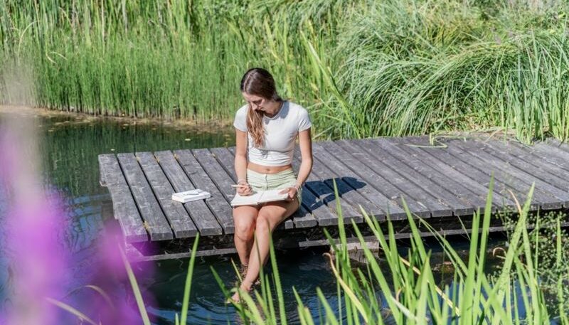 Junge Frau schreibt am Teich.