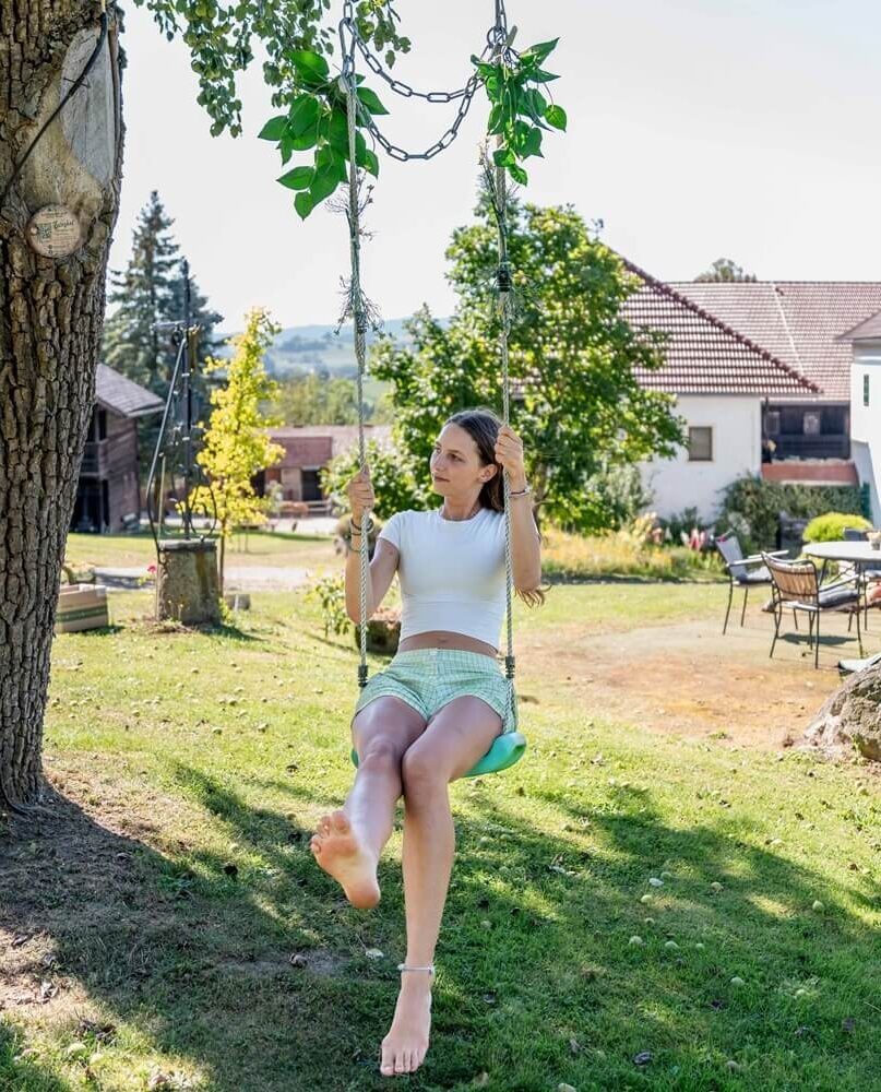 Frau schwingt im Garten auf Schaukel.