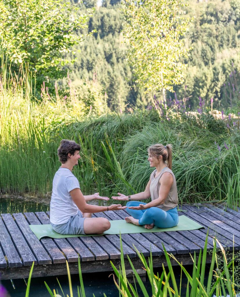 Zwei Personen meditieren am Teich.